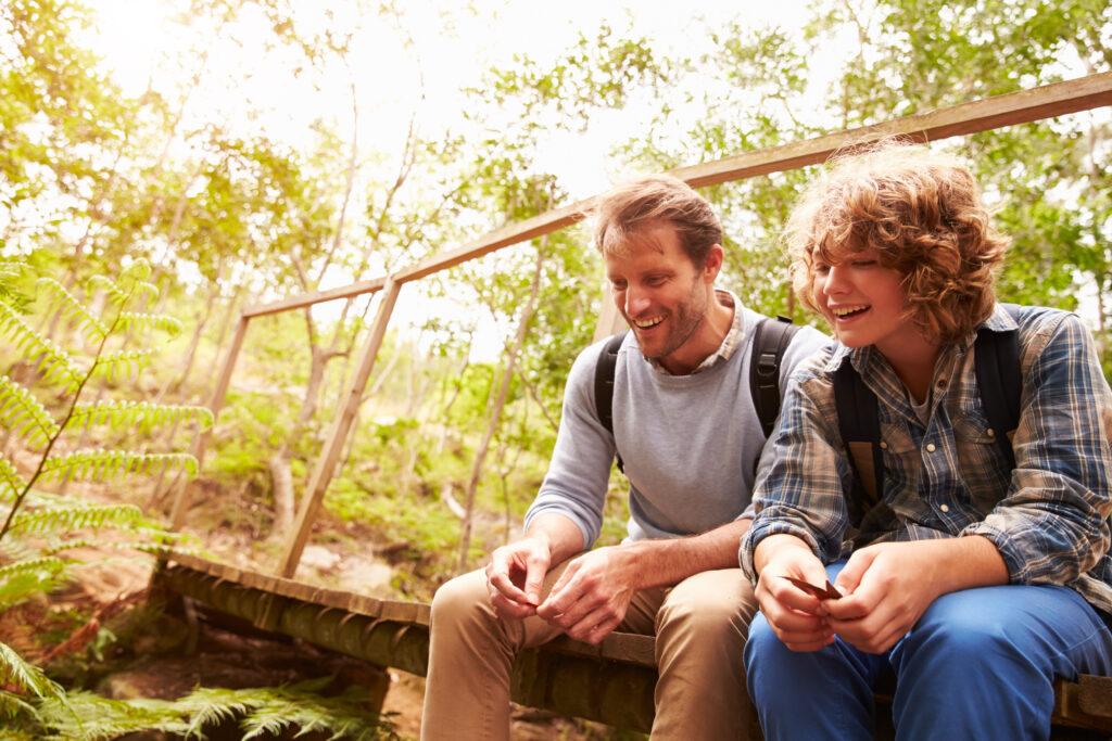 Father and son sitting on a bridge in a forest, close up