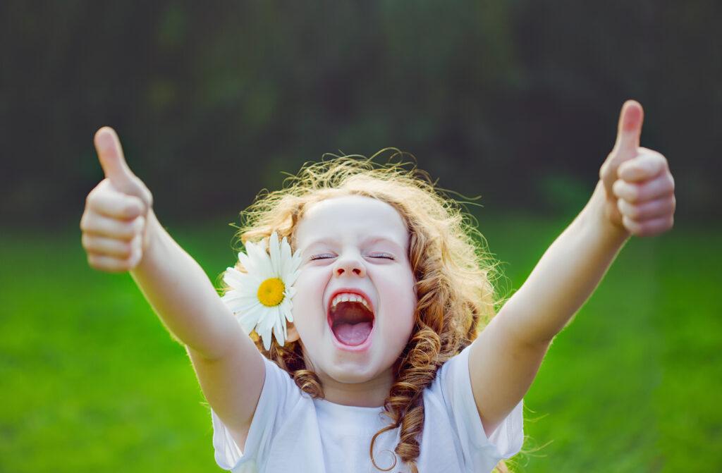 Laughing girl with daisy in her hairs, showing thumbs up.