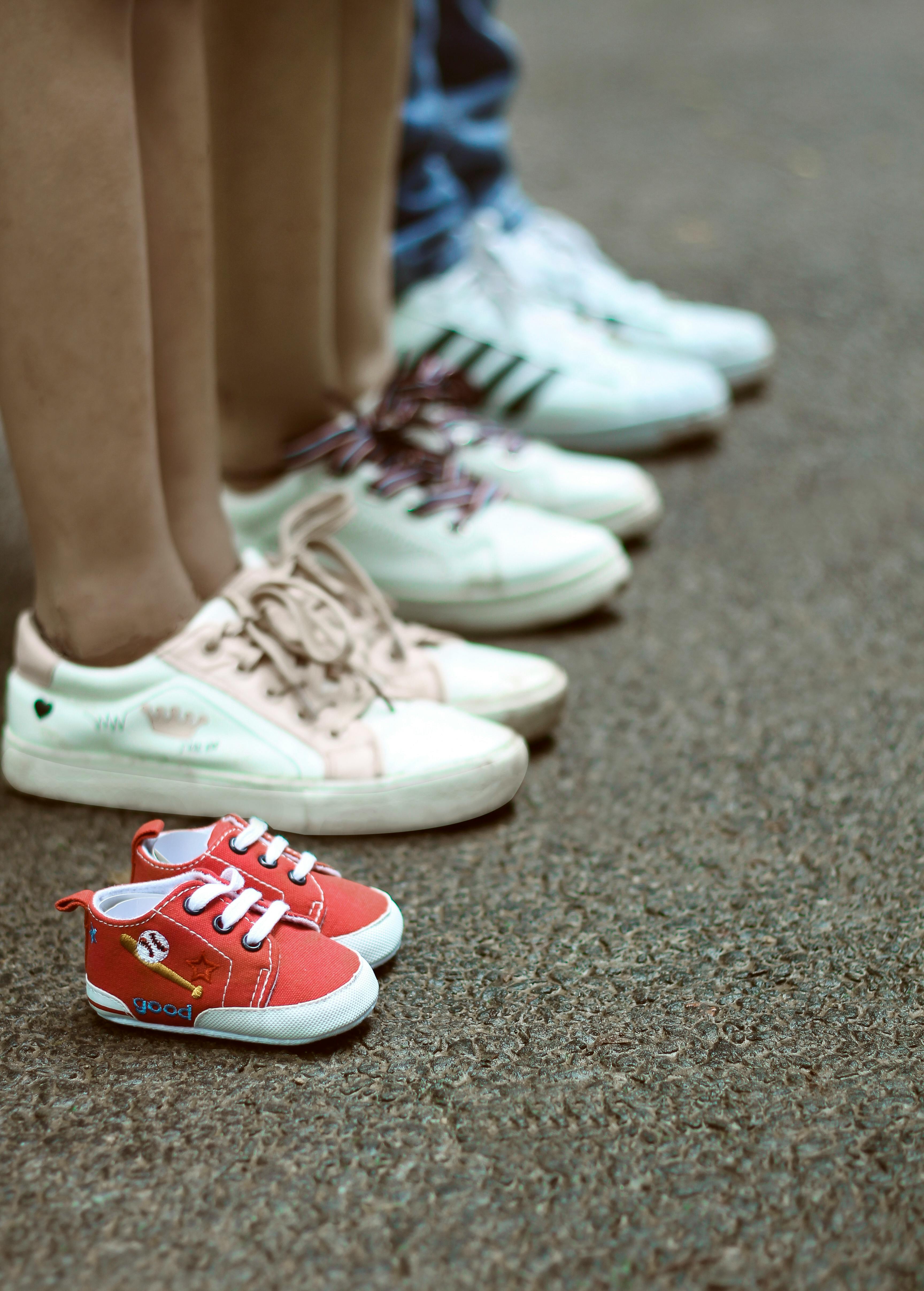 Family shoes lined up on pavement with baby sneakers, symbolizing growth and family bond.