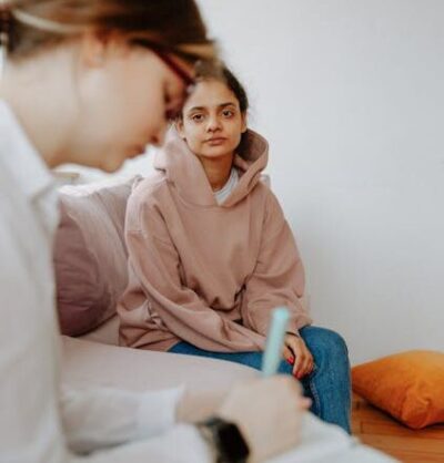 Therapist taking notes while young woman shares her thoughts in a counseling session.