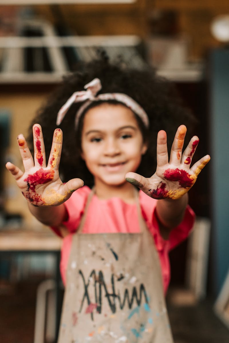 Smiling young girl showing painted hands, capturing childhood creativity and joy.