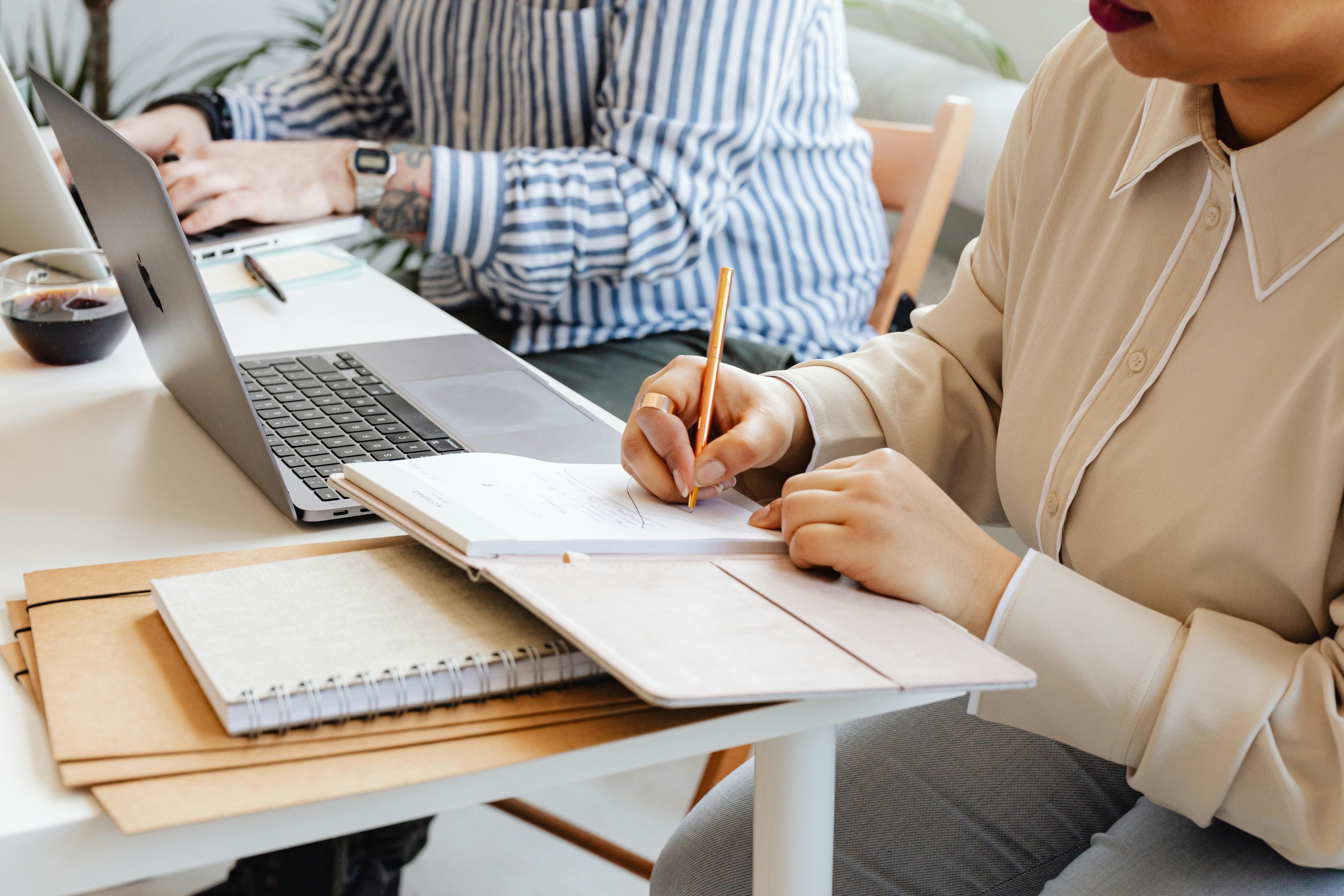 Two individuals working together at a desk with laptops and notebooks, emphasizing teamwork.