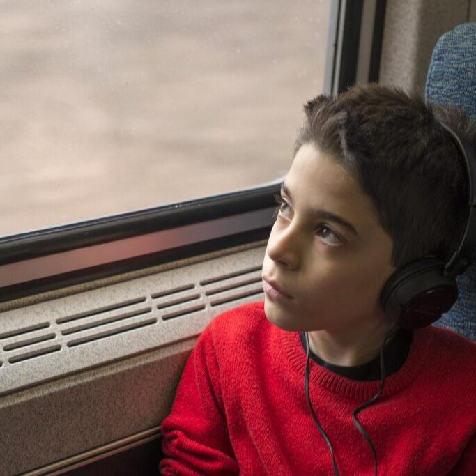 A fourth grader listens to his music while looking out the trains window.